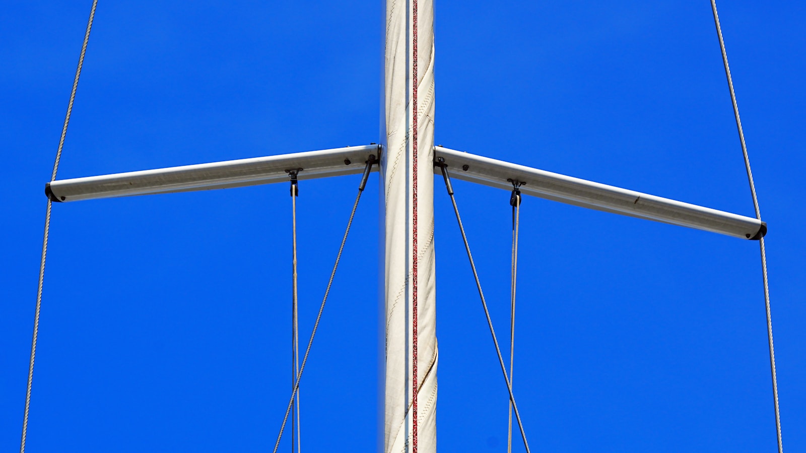 Sailboat mast, spreaders, shrouds, and fittings against a blue sky